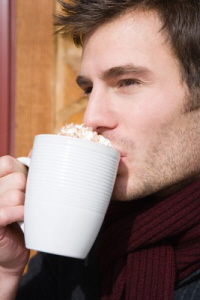 Man drinking a cup of creamy hot chocolate.